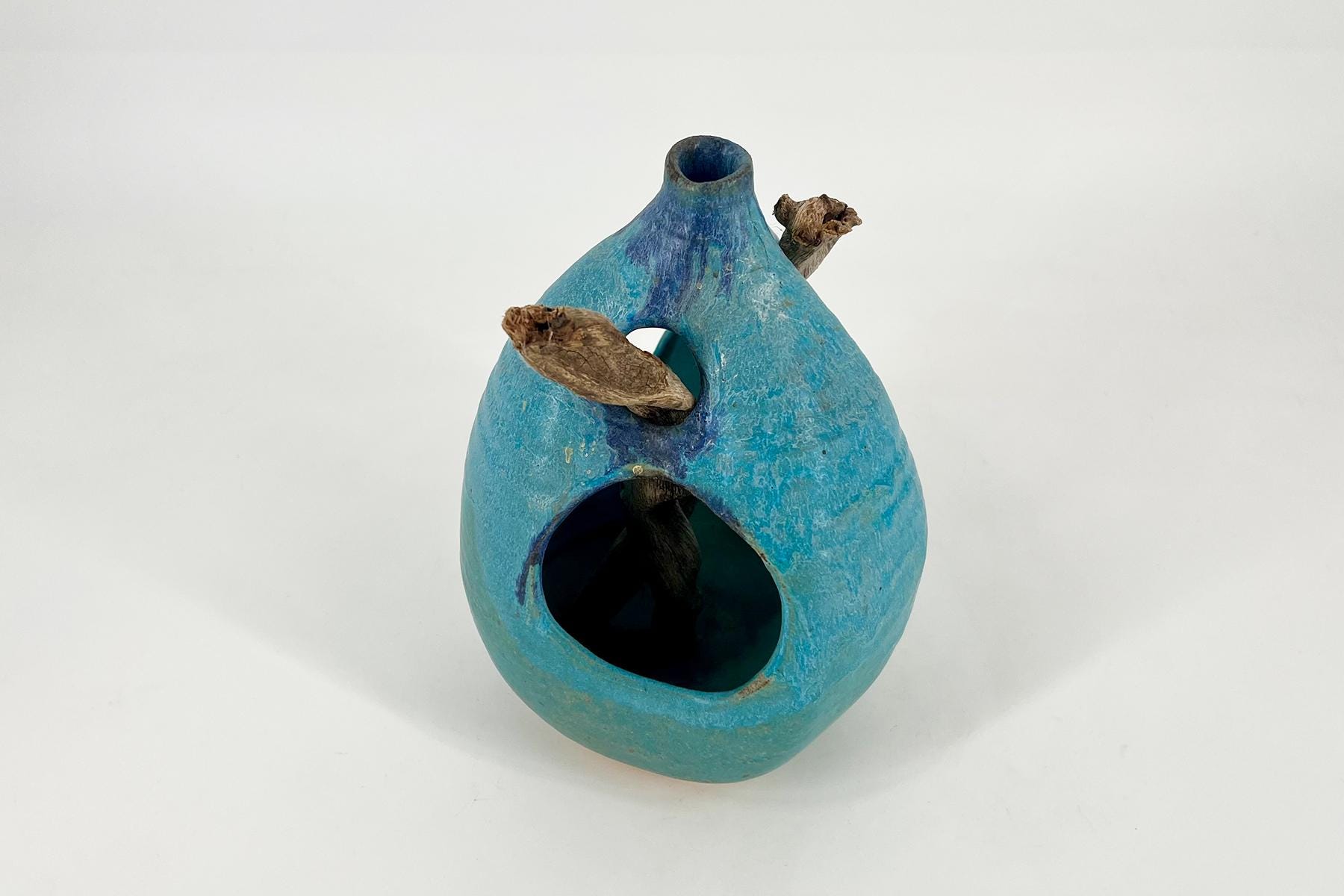 Blue glazed ceramic vase with a wide bottom, circular opening, and dried plant stems protruding from a side hole.