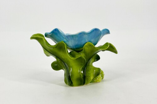 Abstract glass sculpture of a blue flower with twisting green stems on a white background, resembling coral or seaweed form
