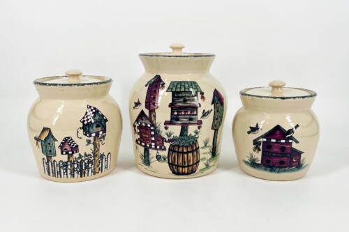 Three cream-colored ceramic jars with lids, each adorned with colorful whimsical village houses on a white background.