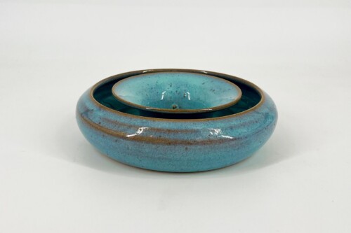Two turquoise glazed ceramic bowls nested together on a white background, with brown rims and glossy finish.